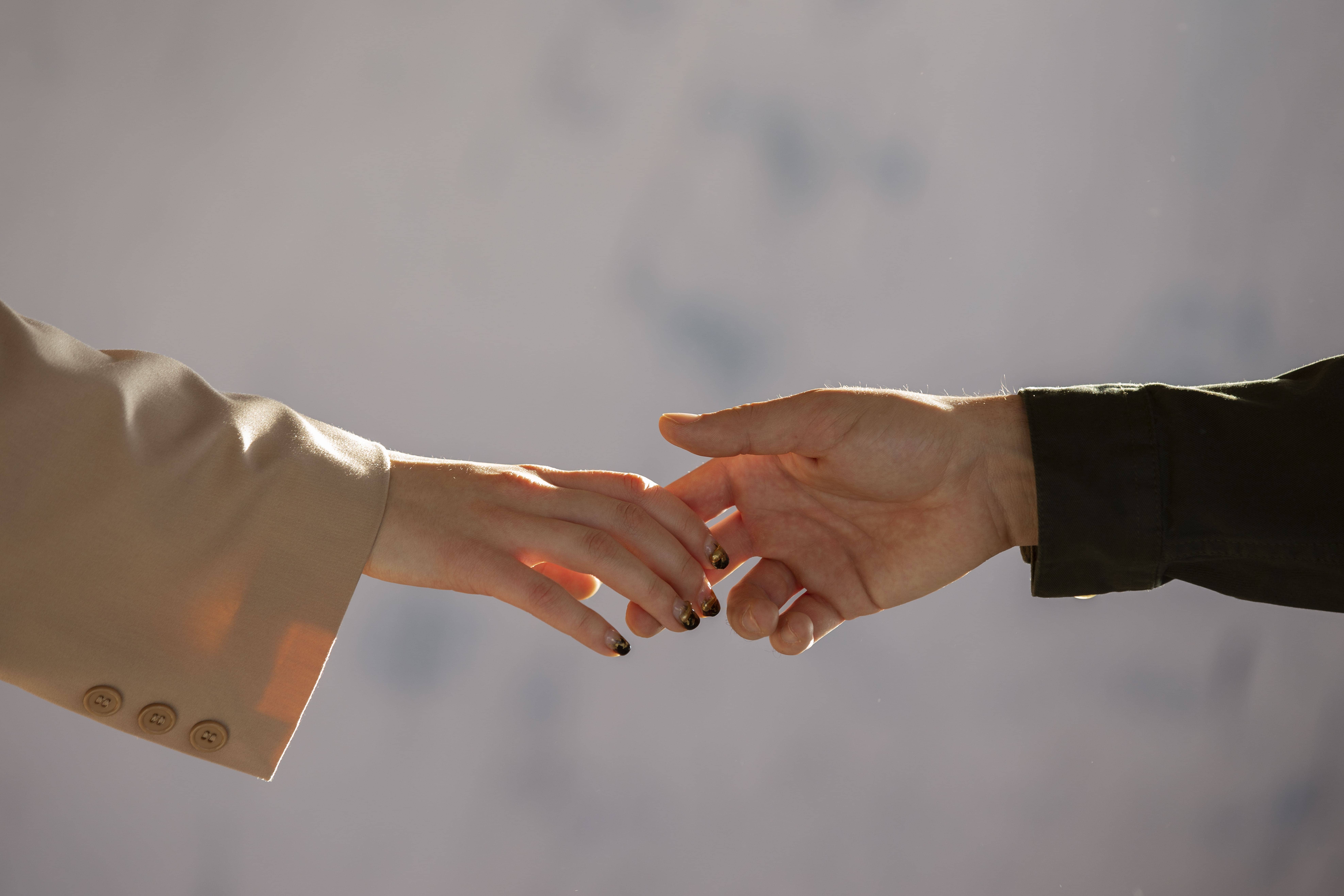 На фото на світлому фоні зображені дві руки, які краєчками пальців тримаються одна за одну. Ймовірно, одна рука чоловіча, а інша жіноча.