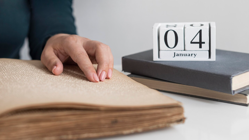 На фото зображена жіноча рука, яка лежить на розгорнутій книзі. Збоку дерев'яний календар із датою 2 січня.