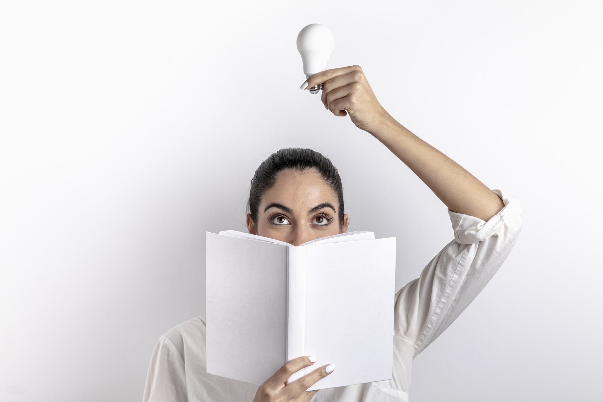 На фото зображена жінка, яка однією рукою тримає над головою білу лампочку, а іншою - книгу, прикриваючи нею половину обличчя.