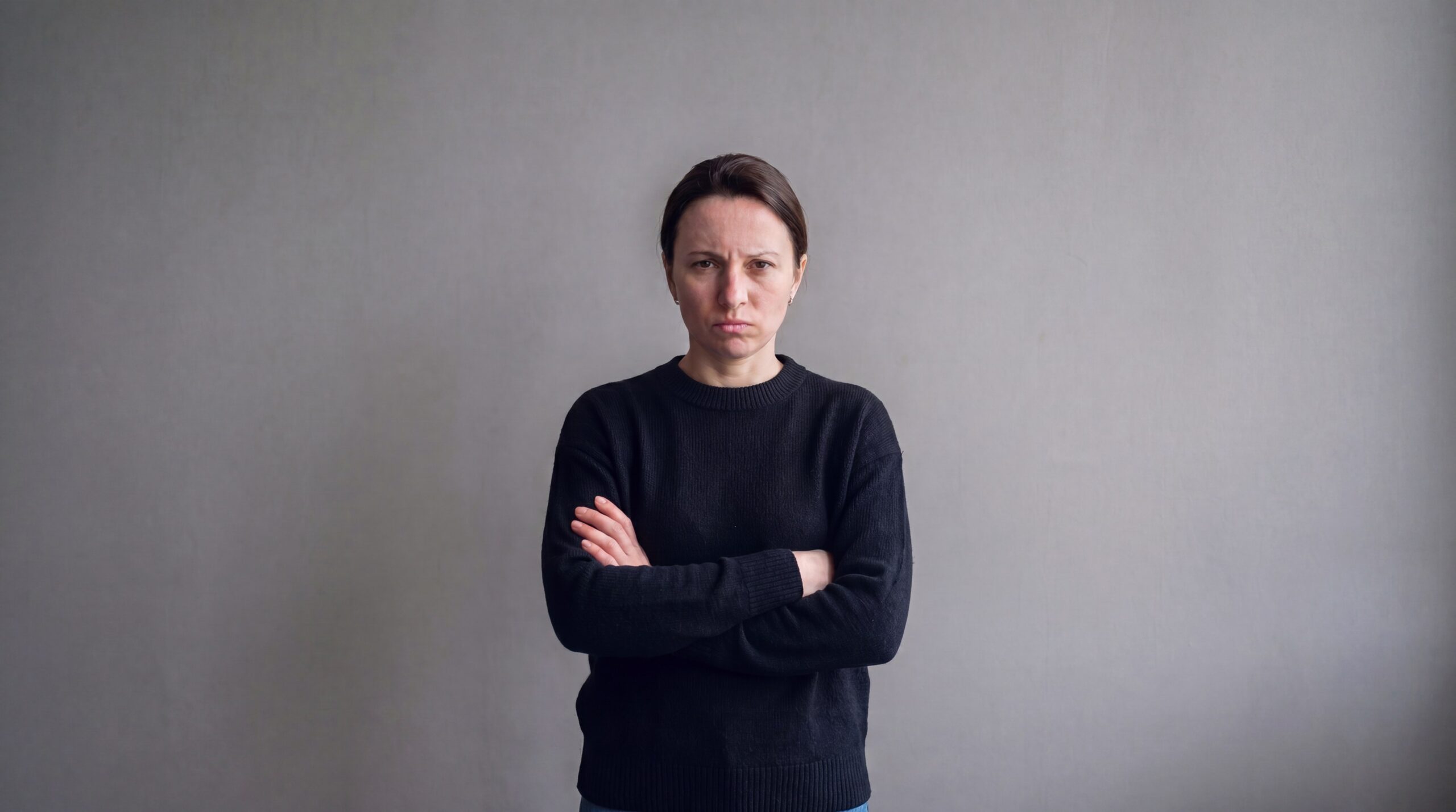 Жінка стоїть зі схрещеними руками та роздратованим виразом обличчя